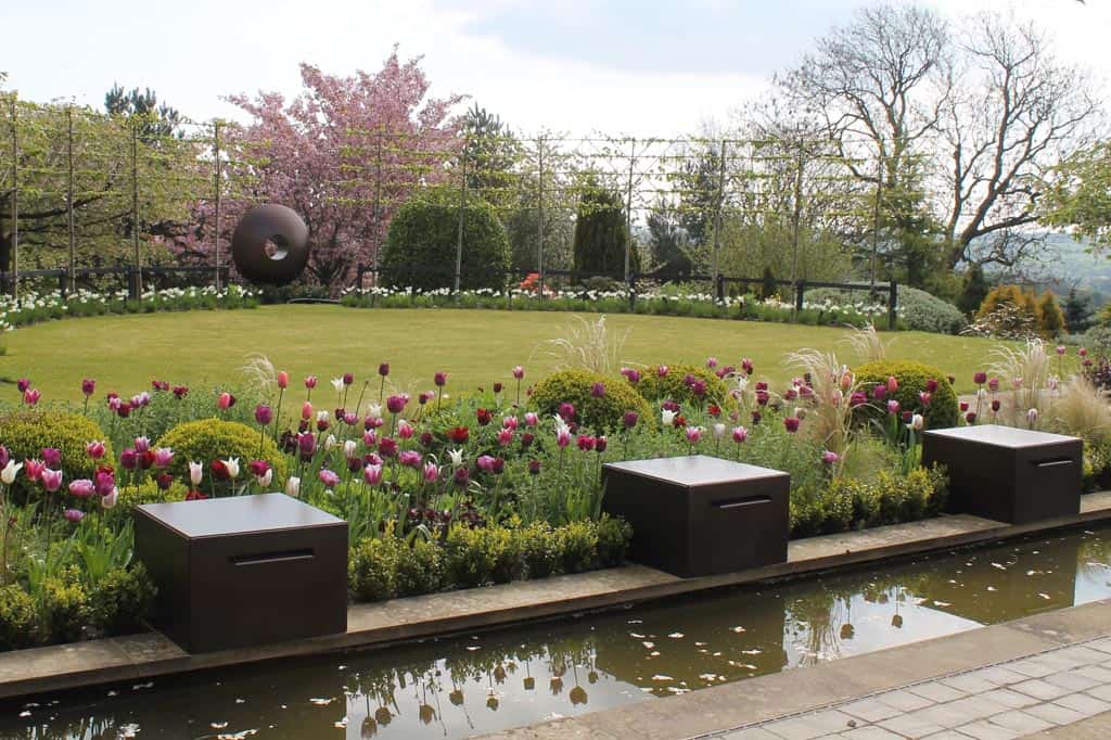 Looking across the water feature and fountains towards the sculpture which sits between a semi circle of pleached trees with rural views in the distance