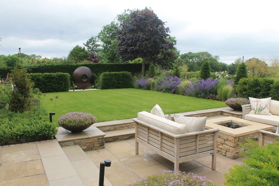 View across a small modern country garden with outdoor sofas, perfect lawn and herbaceous borders this garden look out on beautiful views.