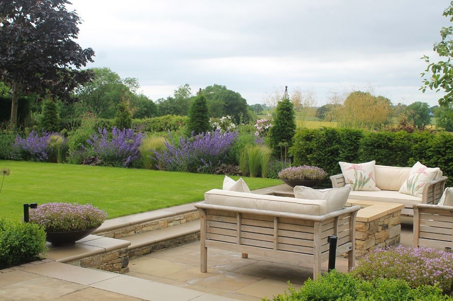 View across a small modern country garden with outdoor sofas, perfect lawn and herbaceous borders this garden look out on beautiful views.